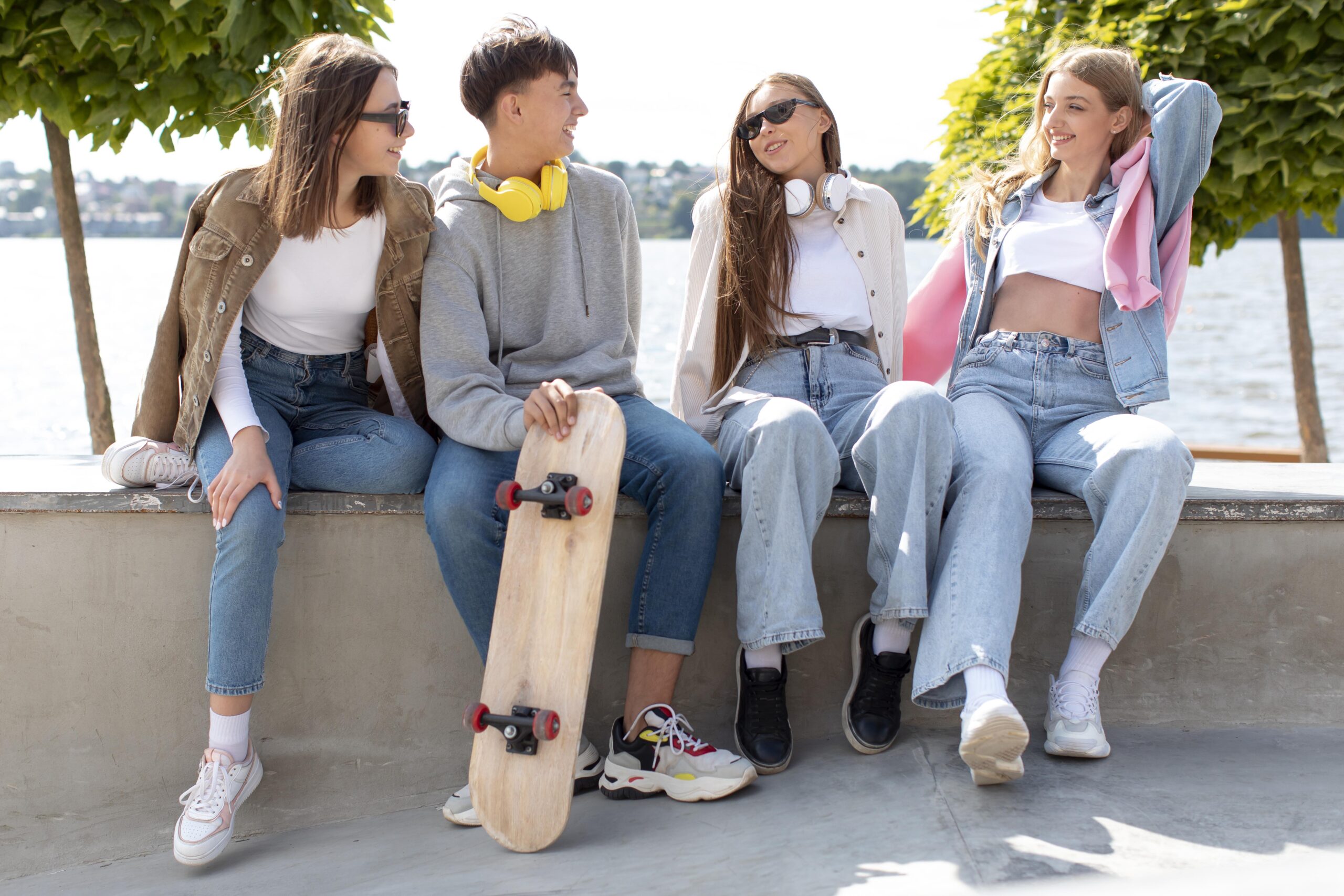 Skupina tinejdžera sjedi na otvorenom s skateboardom, smiju se i razgovaraju, prikazujući prijateljstvo i mladenačku energiju.