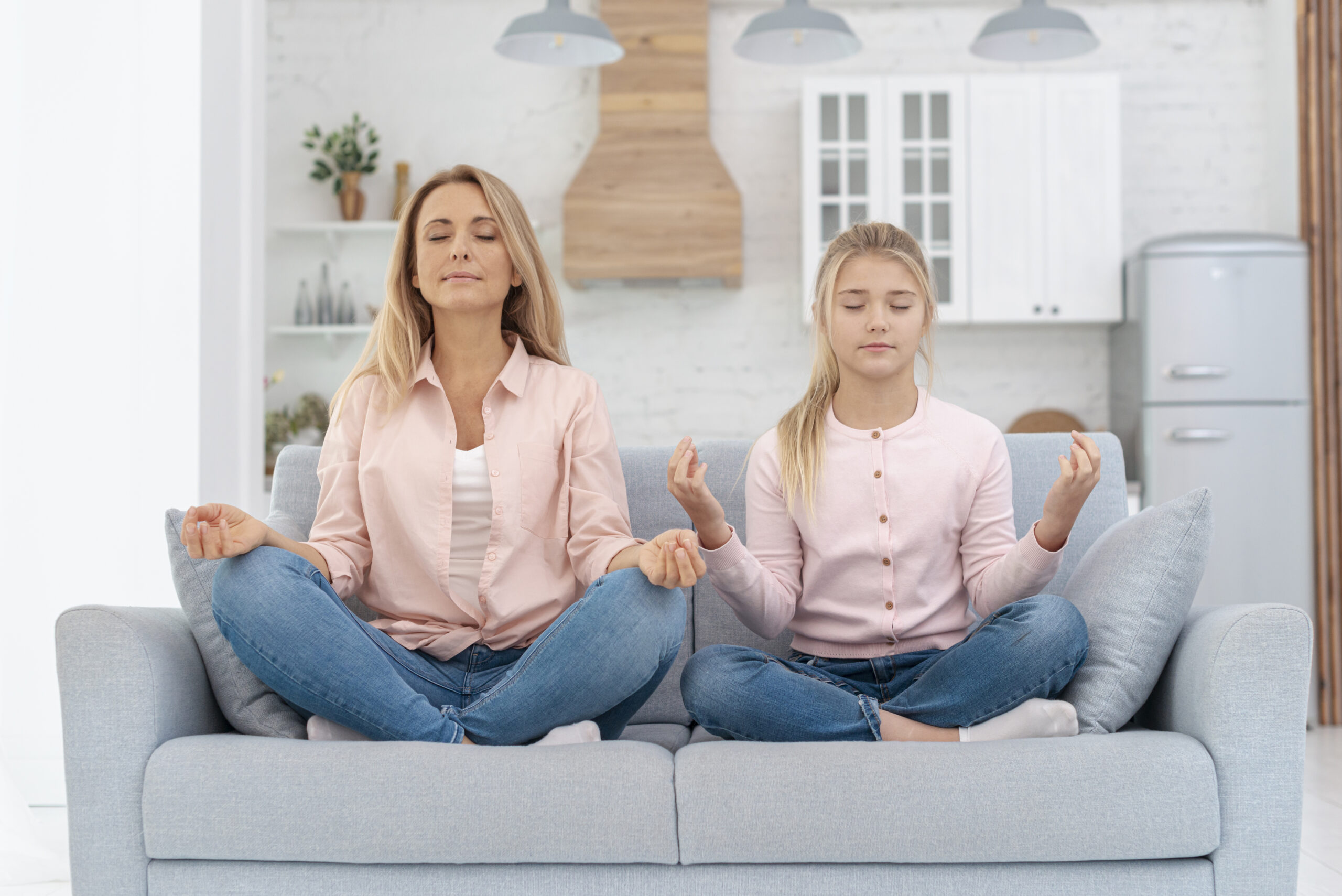 Majka i kći zajedno prakticiraju meditaciju na sofi u mirnom kućnom okruženju, potičući opuštanje i svjesnost.