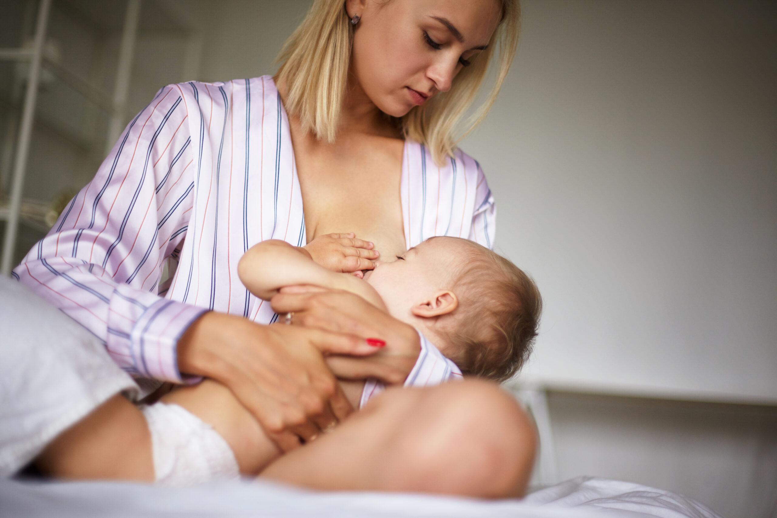 Majka u pidžami sjedi na krevetu i doji bebu, pružajući toplinu i sigurnost tijekom hranjenja.